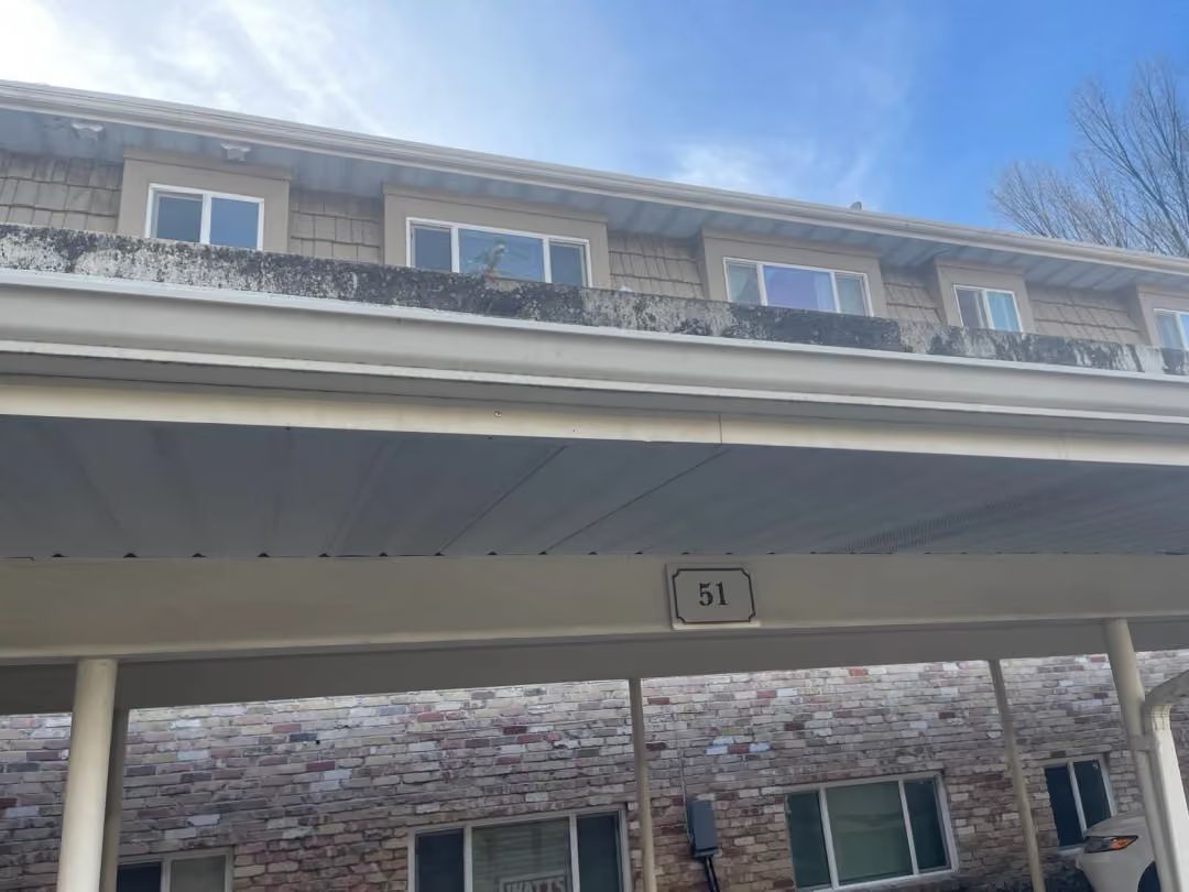 Covered parking area beneath a stone apartment building with a clear blue sky above