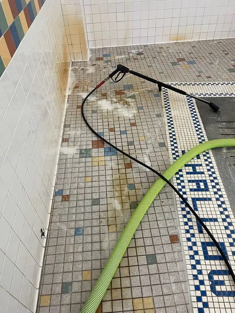 Pool deck with two hoses or cables lying on wet mosaic tiles near the wall