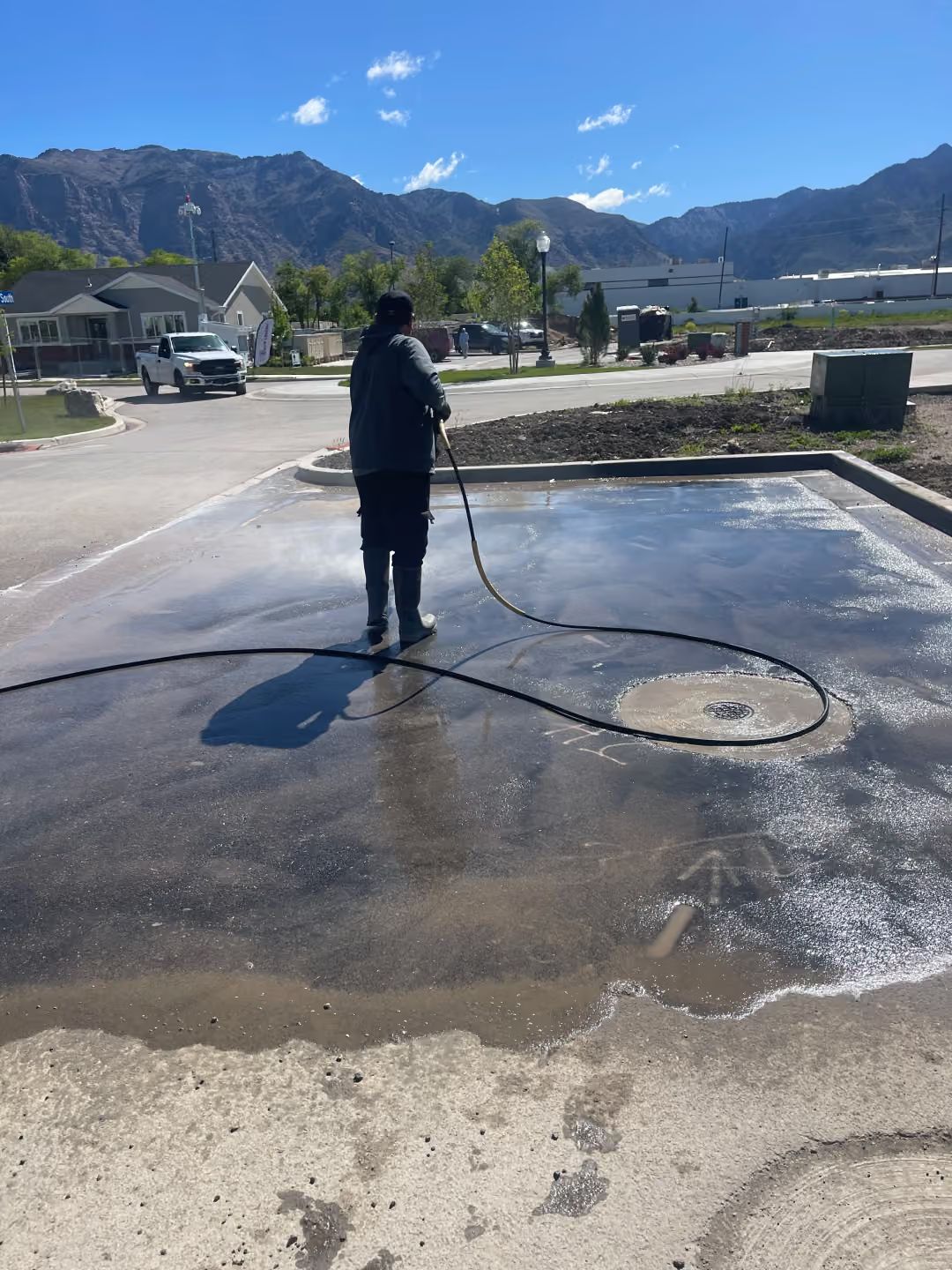 Person pressure-washes wet pavement with mountains in the background.