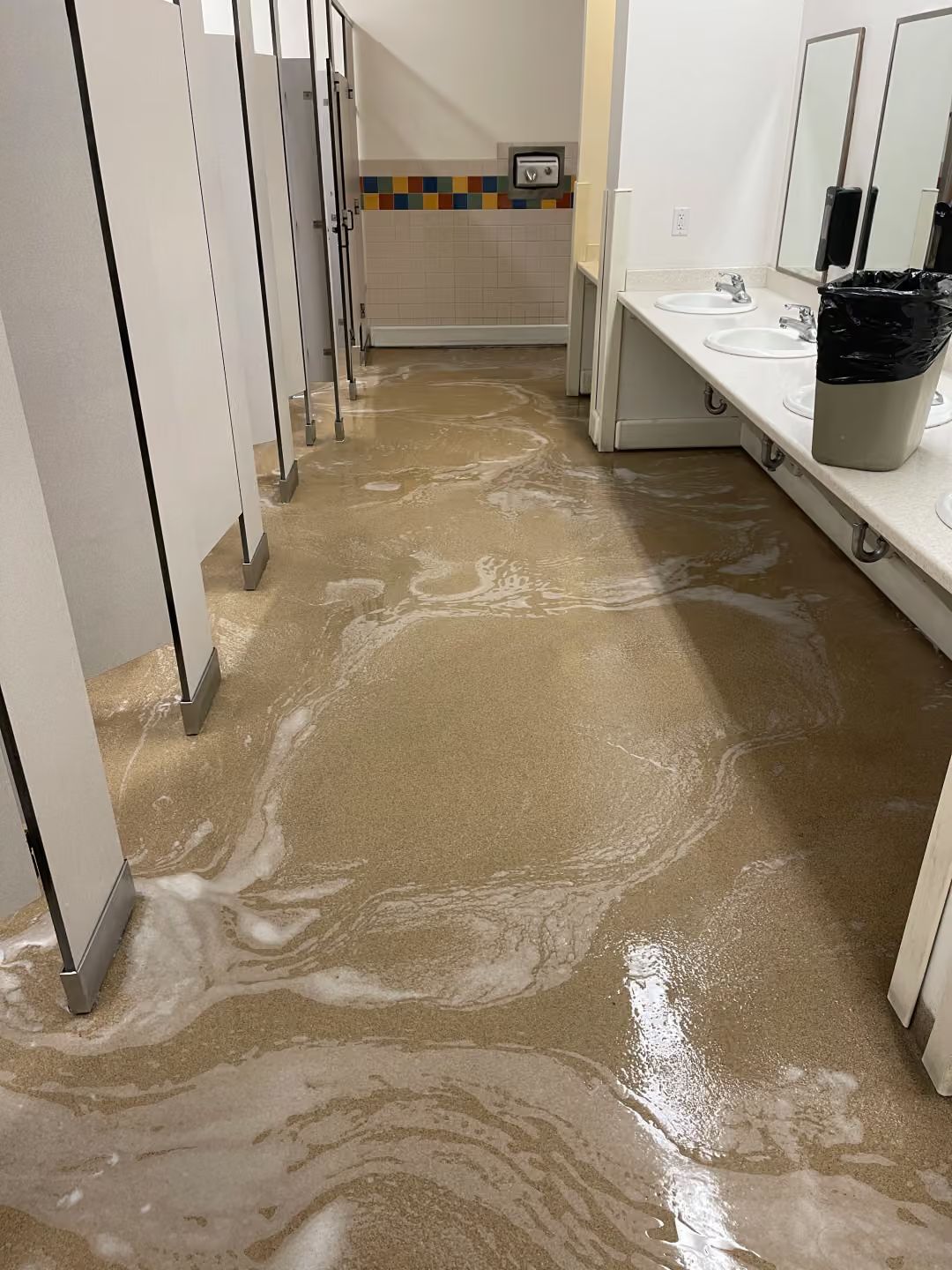 Restroom floor covered in muddy floodwater, with stalls and sinks along the sides.