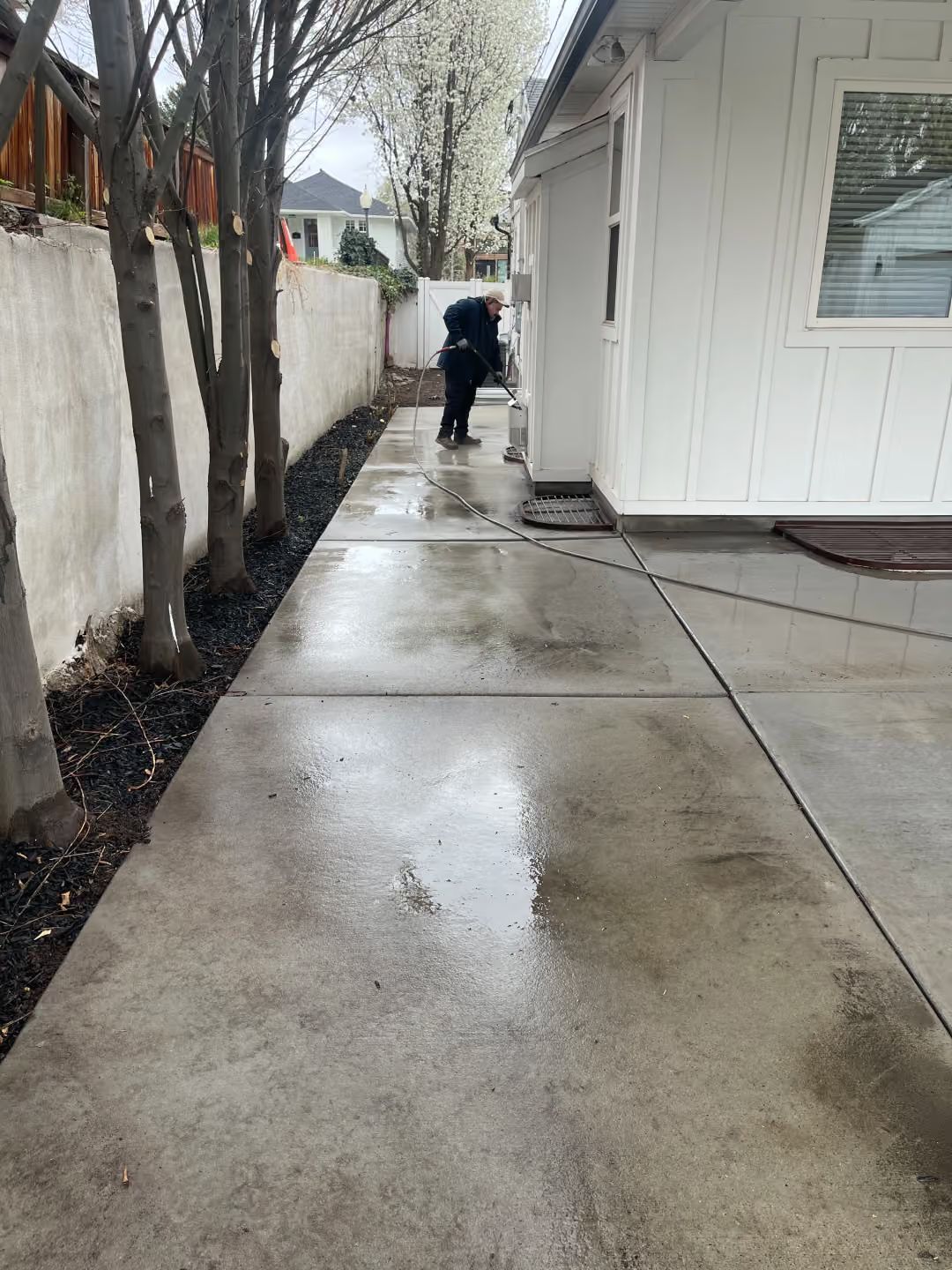 Rainy sidewalk beside white building, with a person walking away at the far end.