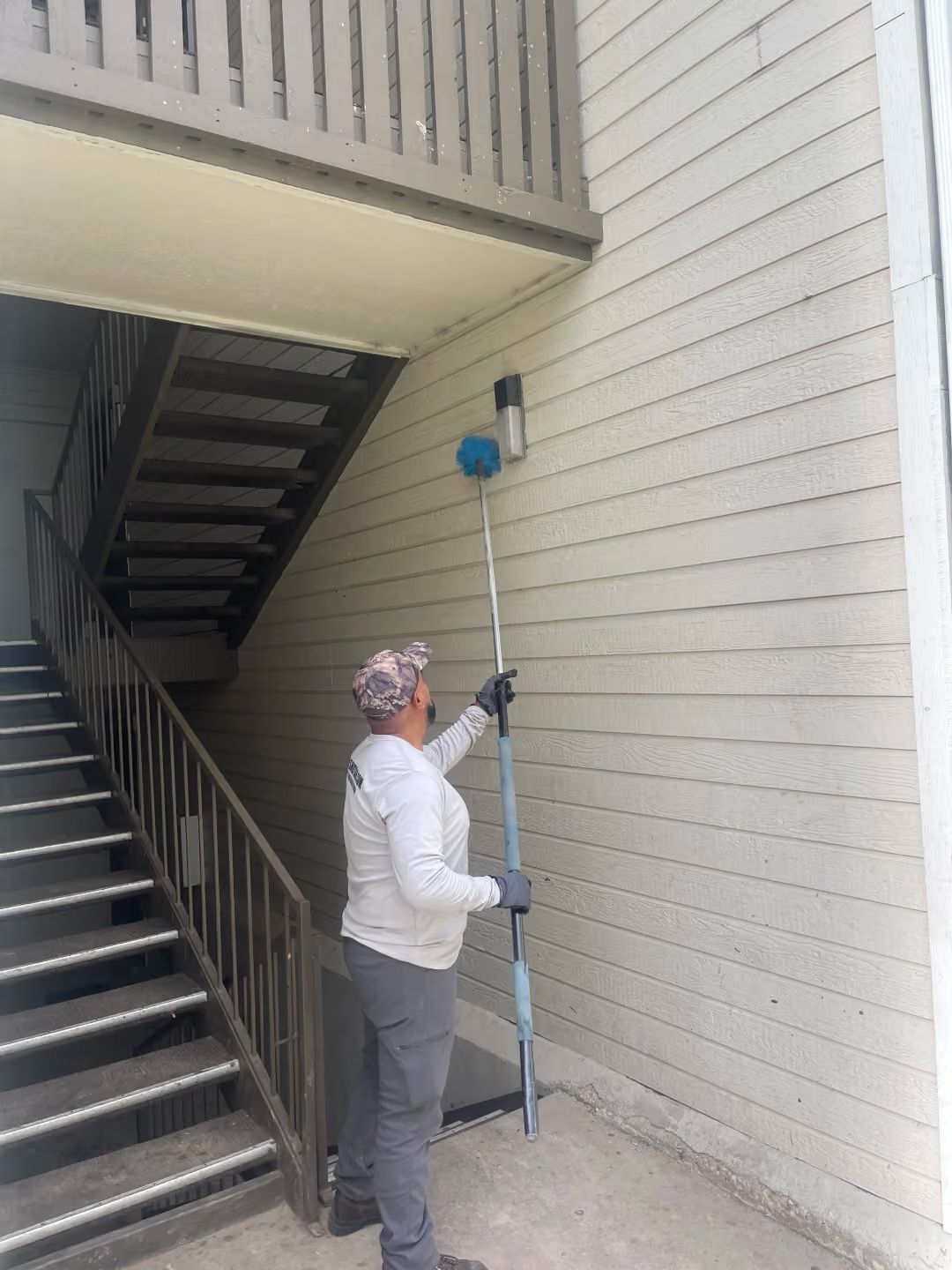 Person measuring the height of a wall with a long pole beside an outdoor stairwell.