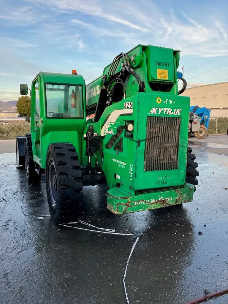 Green forestry machine on wet pavement, viewed from the front-left side.