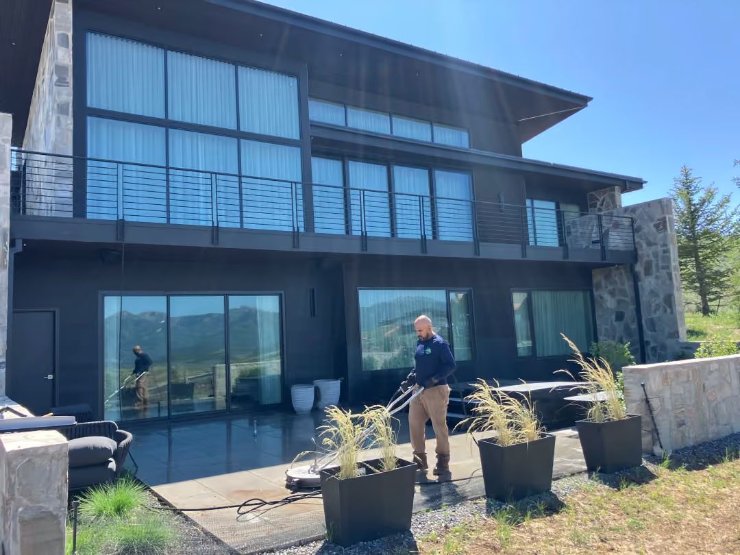Modern two-story house with glass balcony and a person standing on the patio in front of potted plants