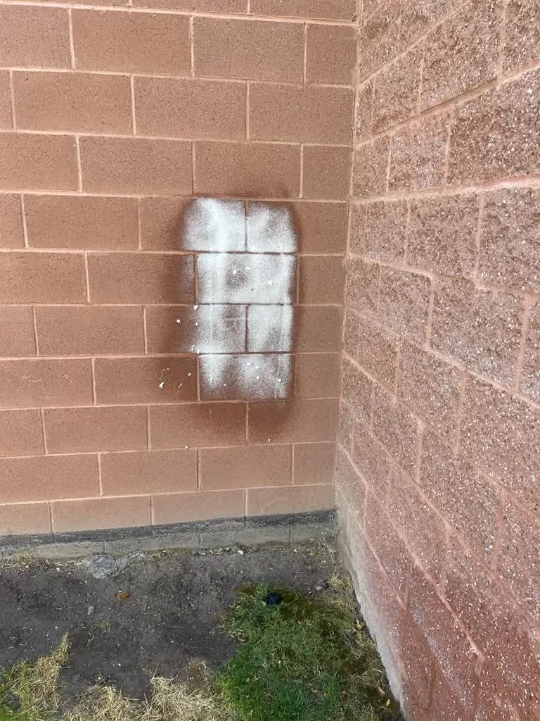 White-painted patch on a brick wall beside a building corner and dark ground.