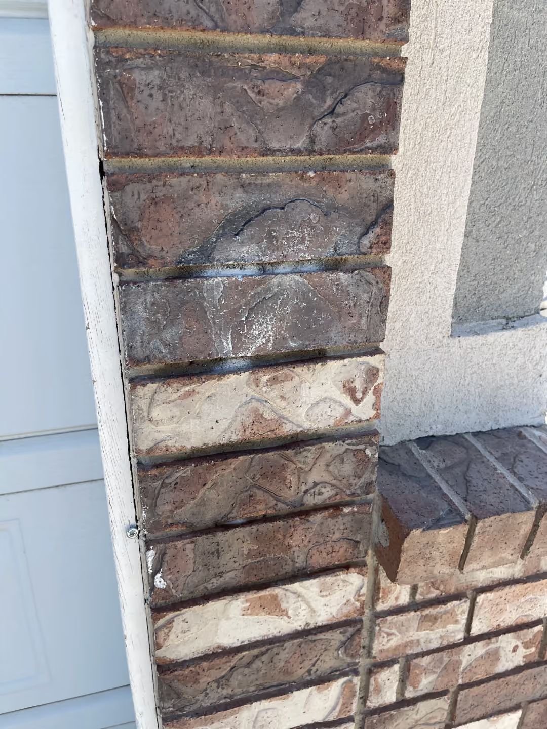 Close-up of a stone pillar and stucco wall beside a white door, with a brick base and white residue on the stones.