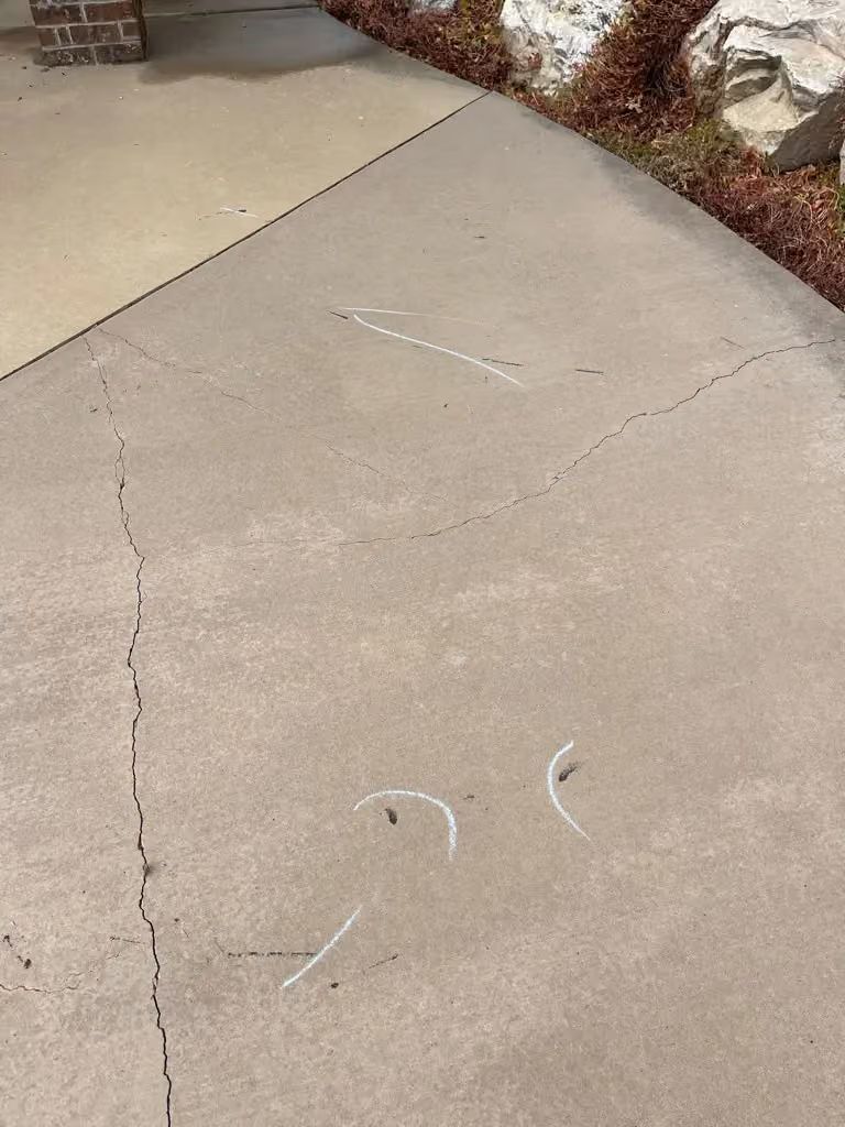 Cracked concrete sidewalk with chalk markings near a landscaped edge