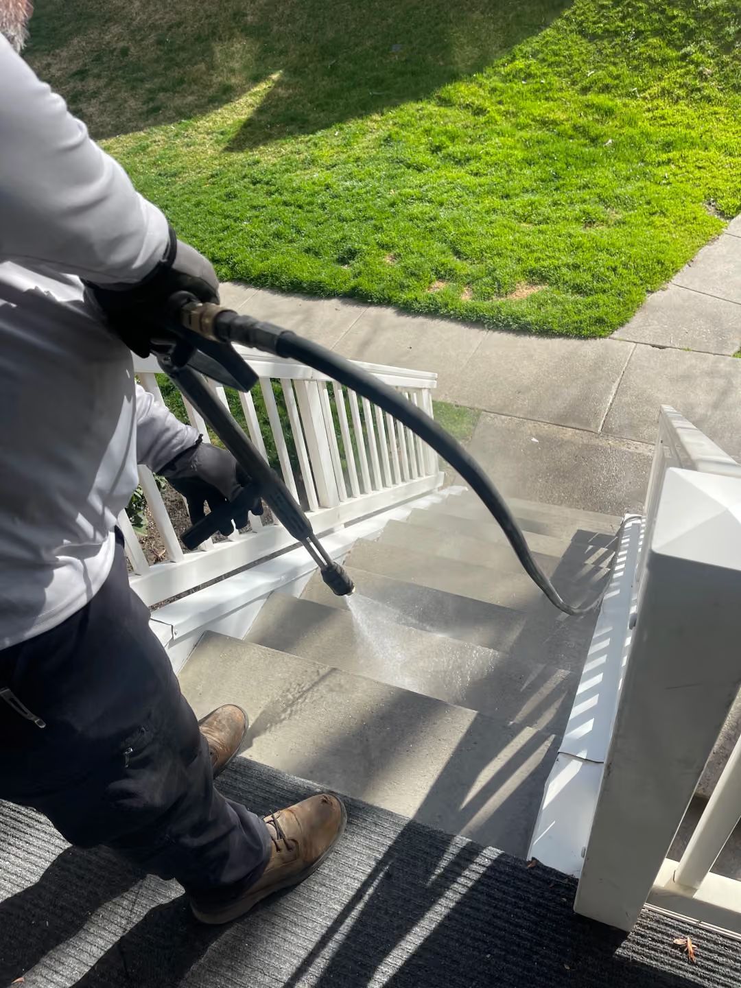 Person using a pressure washer on outdoor concrete steps beside a green lawn