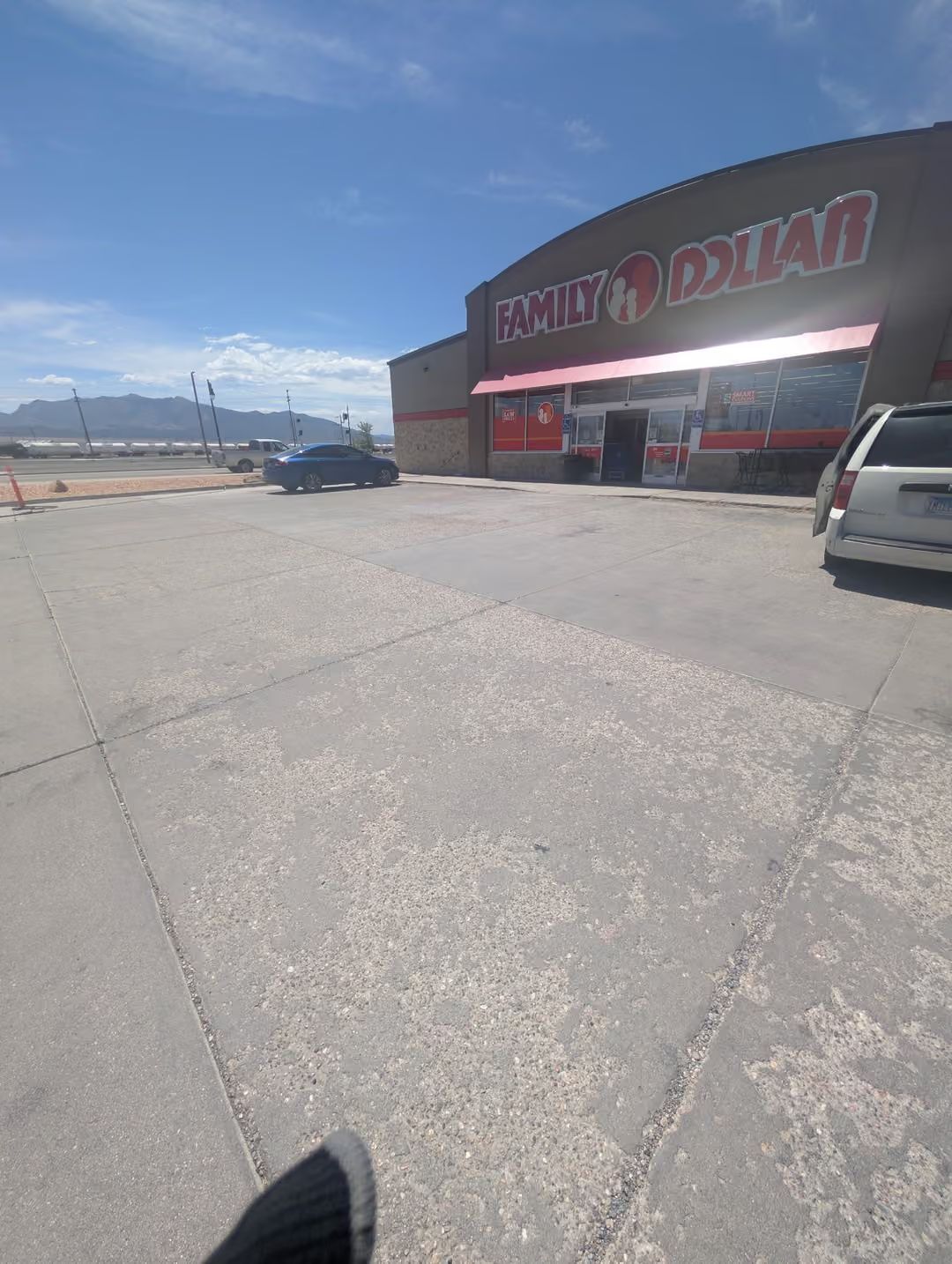 Parking lot outside a red storefront on a sunny day, with cars parked nearby and mountains in the distance