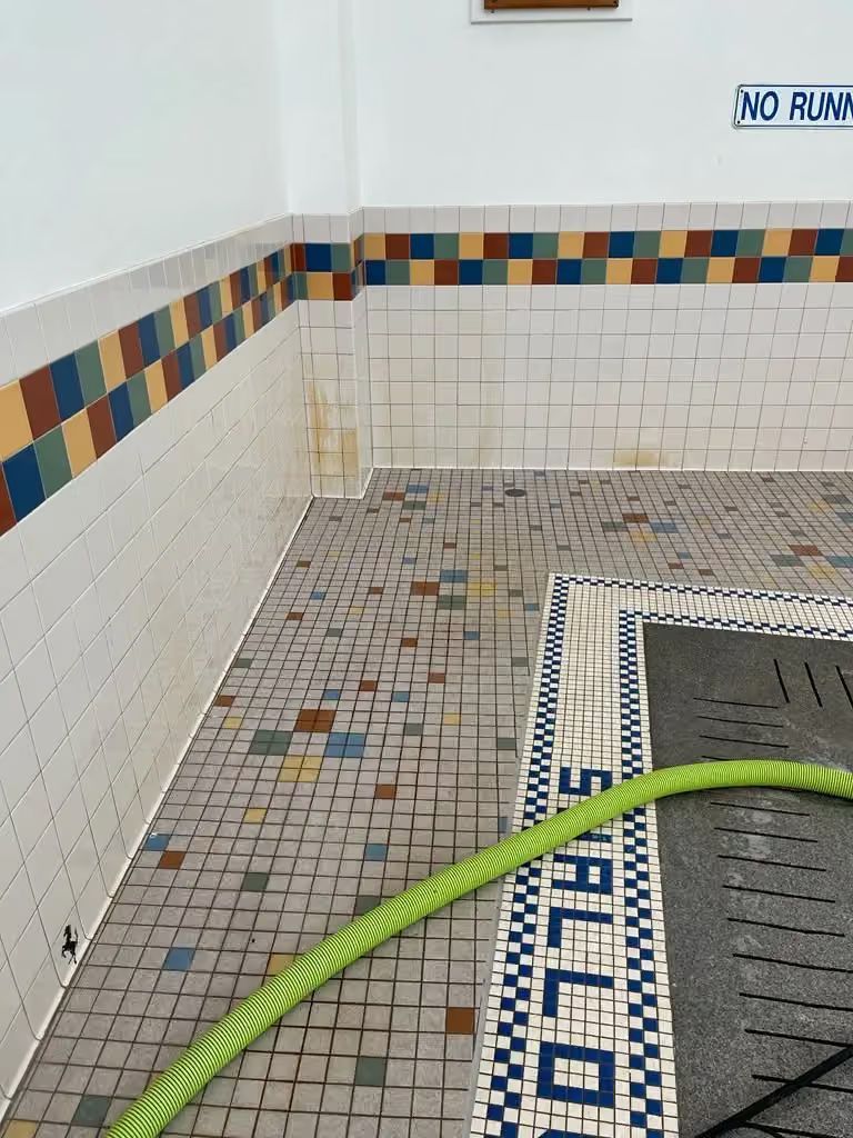 Tiled shower corner with a green hose and a mosaic-patterned floor drain area