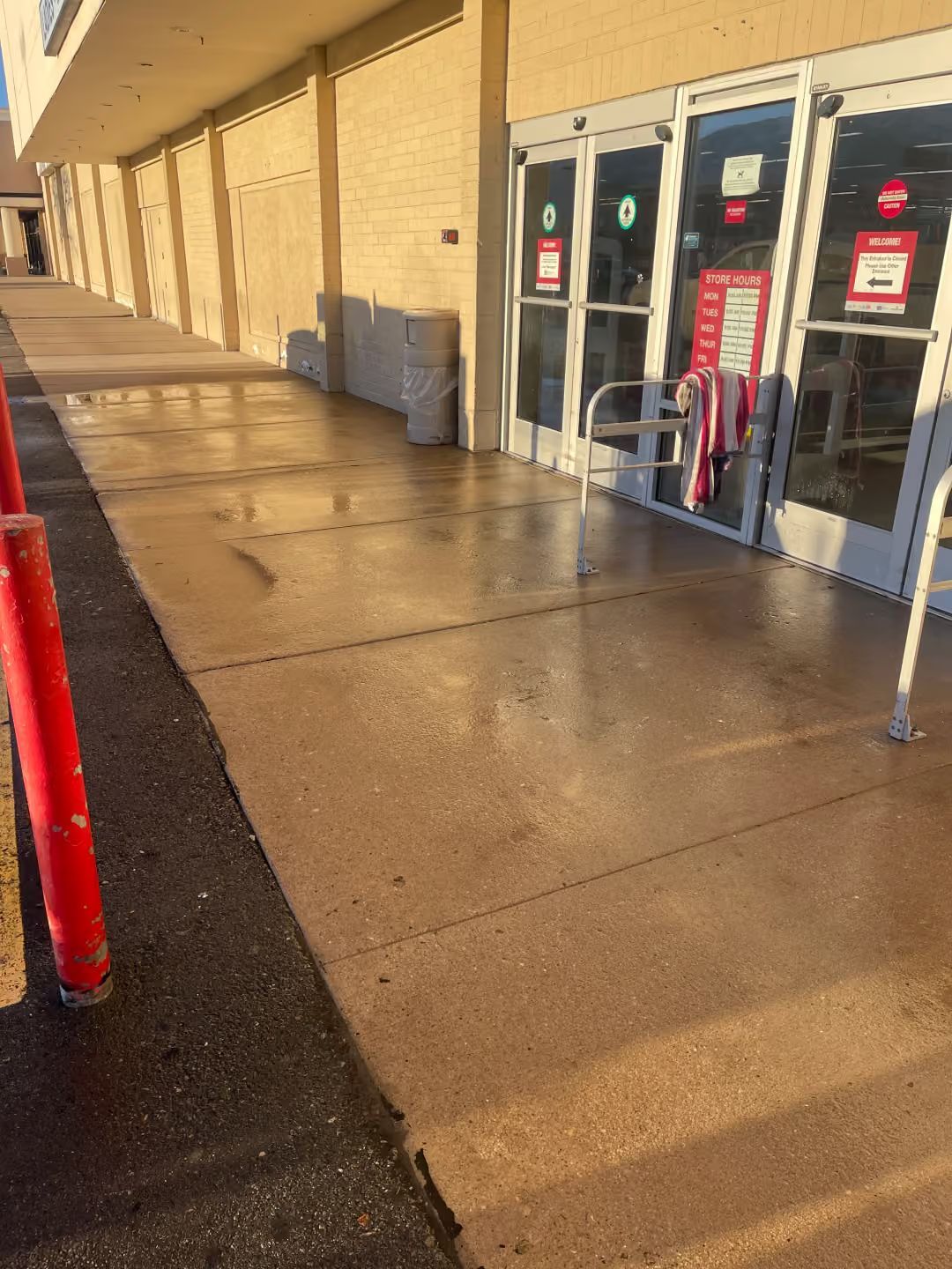 Storefront entrance with glass doors, red cart corral, and wet sidewalk in sunlight