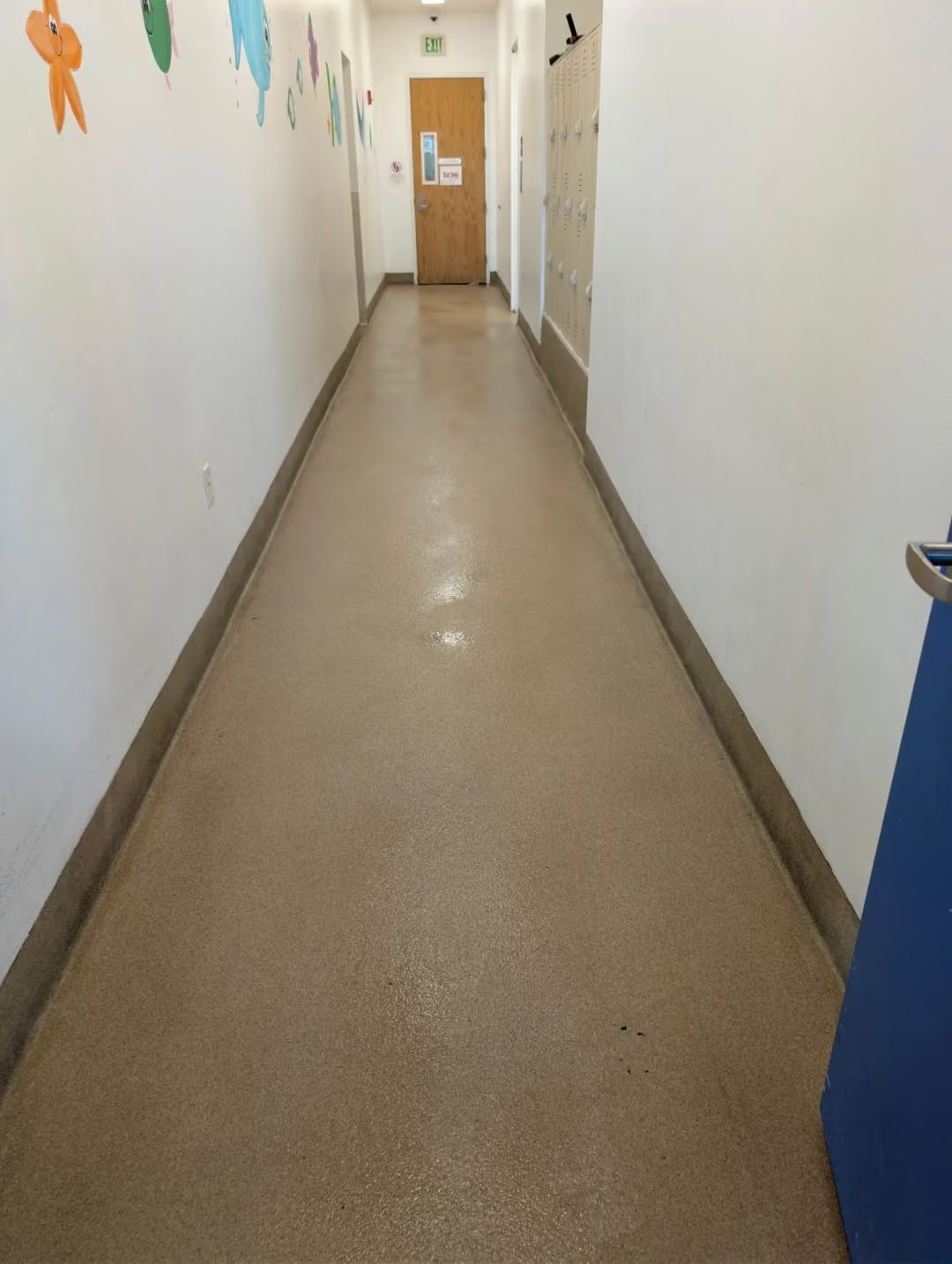 Empty hallway with beige carpet and white walls, leading to a wooden door at the end.