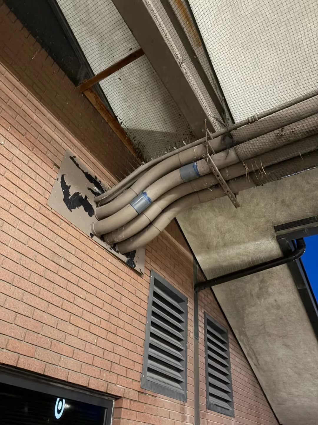 Brick building exterior with exposed pipes and vents under a concrete overhang