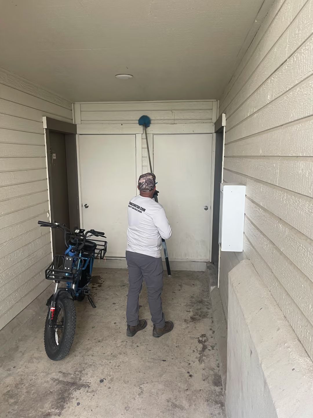Person cleaning a wall in a covered entryway beside a parked motorcycle.