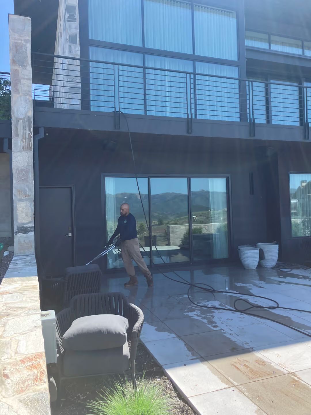 Person standing on a patio outside a modern home with outdoor chairs and potted plants