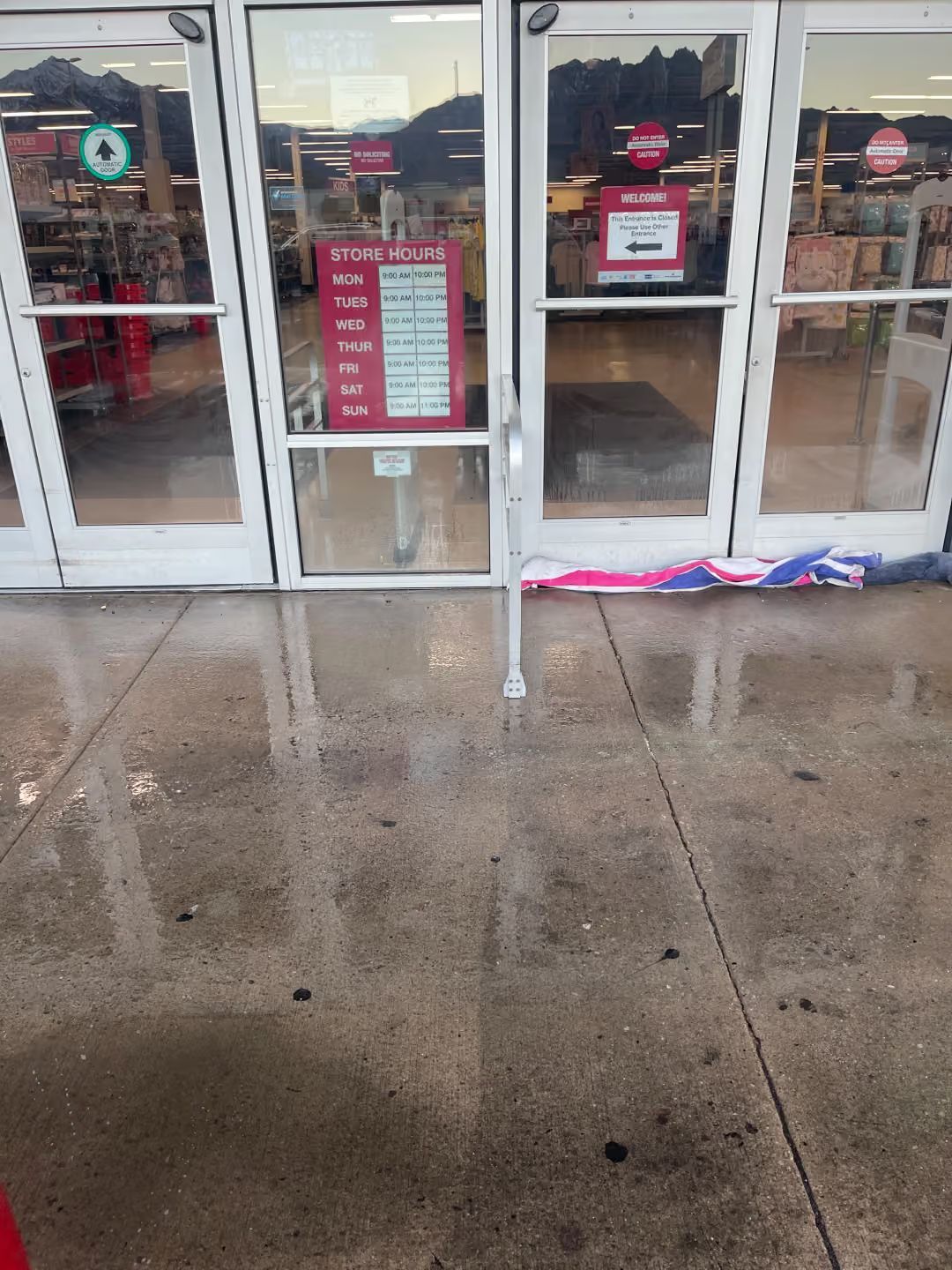 Storefront entrance with wet sidewalk and a small red-white-blue fabric item near the door