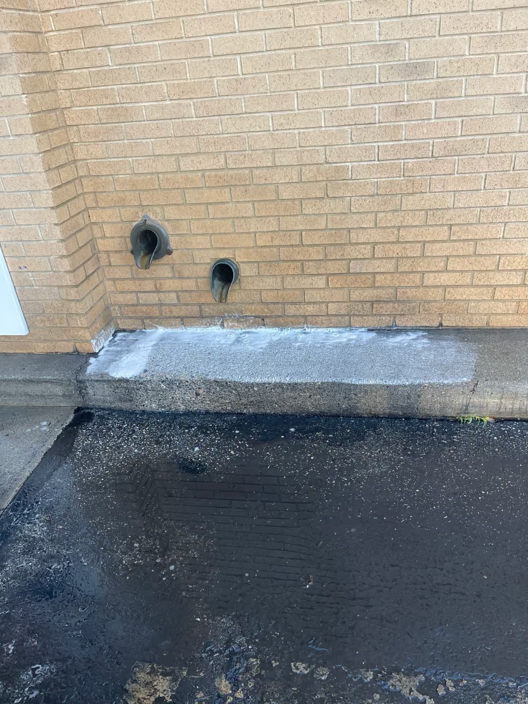 Brick wall with two dark vents above a concrete curb beside wet black pavement.