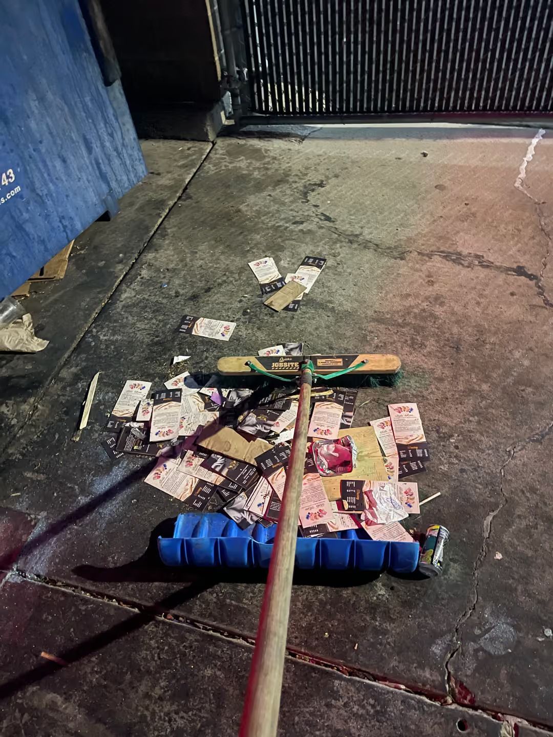 Broom sweeping scattered cash and paper on a concrete sidewalk near a gate