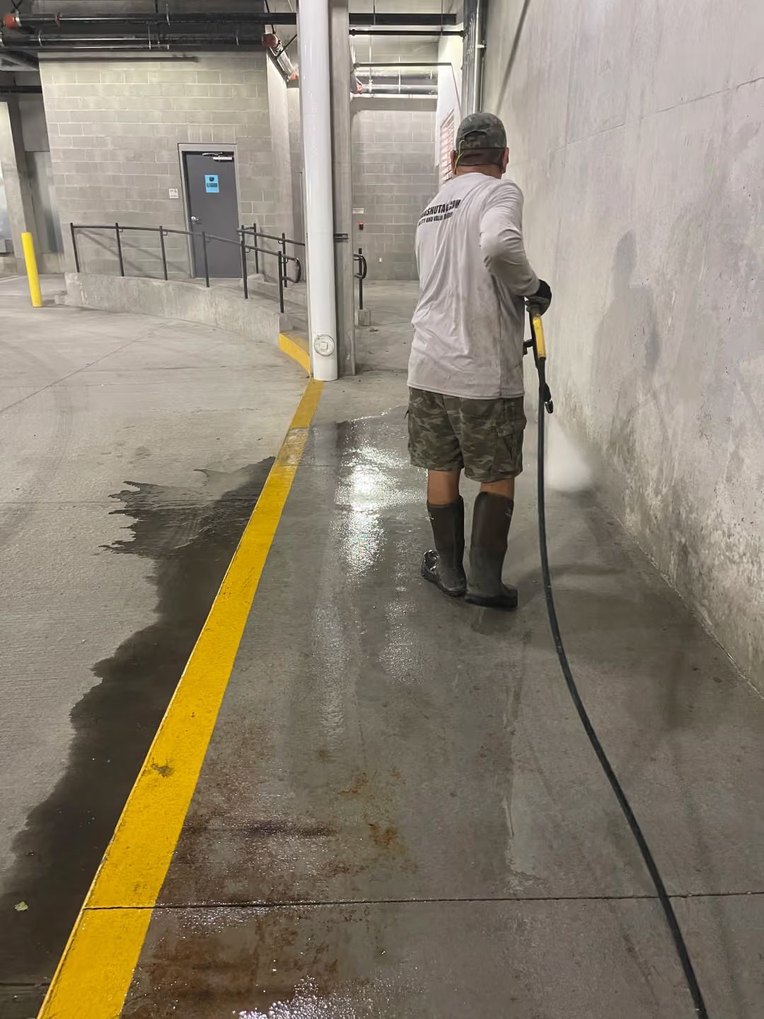 Worker pressure-washing a wet concrete floor in an industrial garage hallway