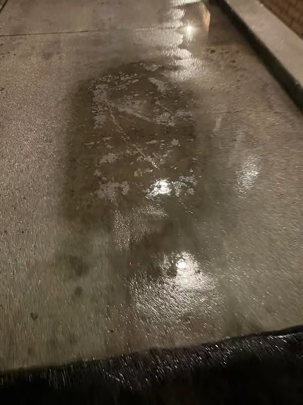 Wet concrete walkway with puddles reflecting light in a dim area