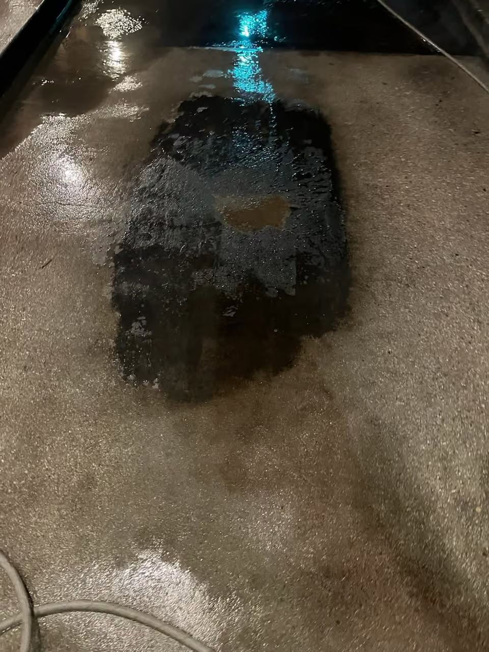 Wet concrete floor with a dark wet patch and a hose on the left side.