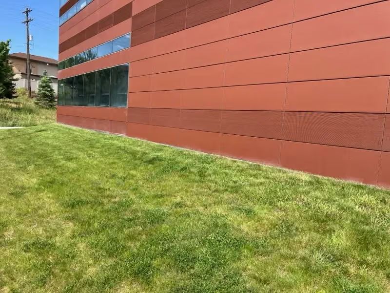 Modern building with orange panels, dark windows, and a grassy lawn beside it
