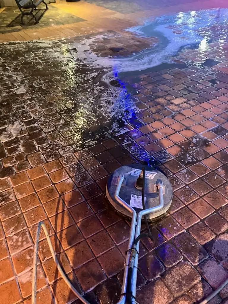 Pressure washer spraying water across a brick patio at night, creating a wet cleaning path.