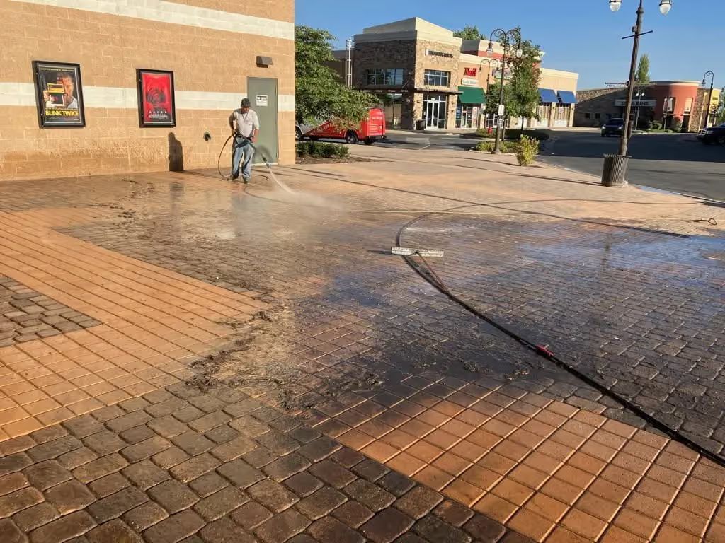 Wet brick plaza with puddles, a person near a brick wall, and shops in the background