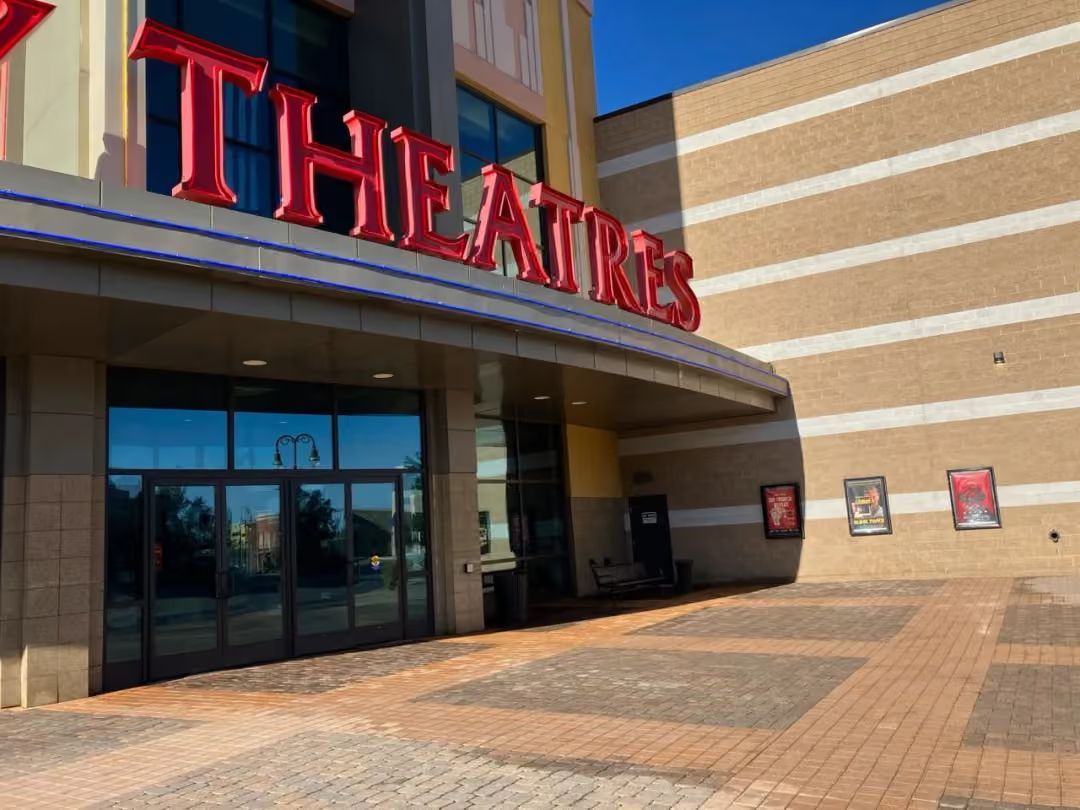 Entrance to a theater with red signage, glass doors, and a brick walkway outside.