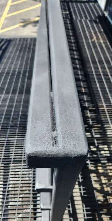 Gray metal bench on a grated walkway, viewed from the end