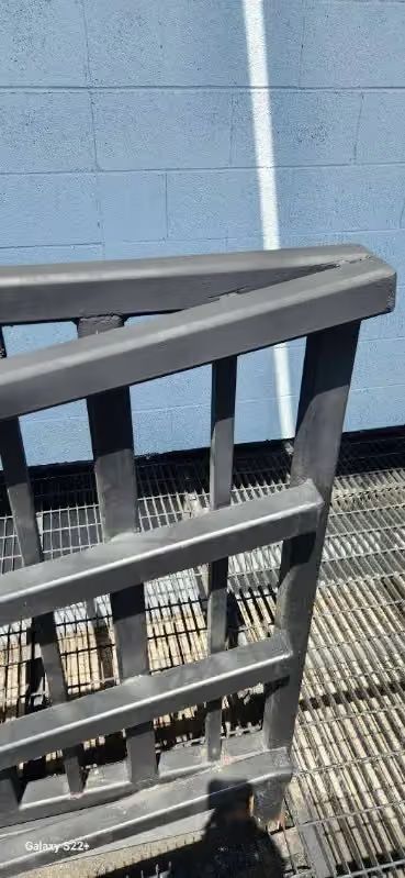 Black railing beside a blue brick wall on a grated metal walkway