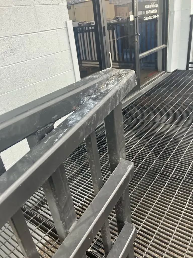 Industrial catwalk with metal grating and a gray railing beside a cinderblock wall.