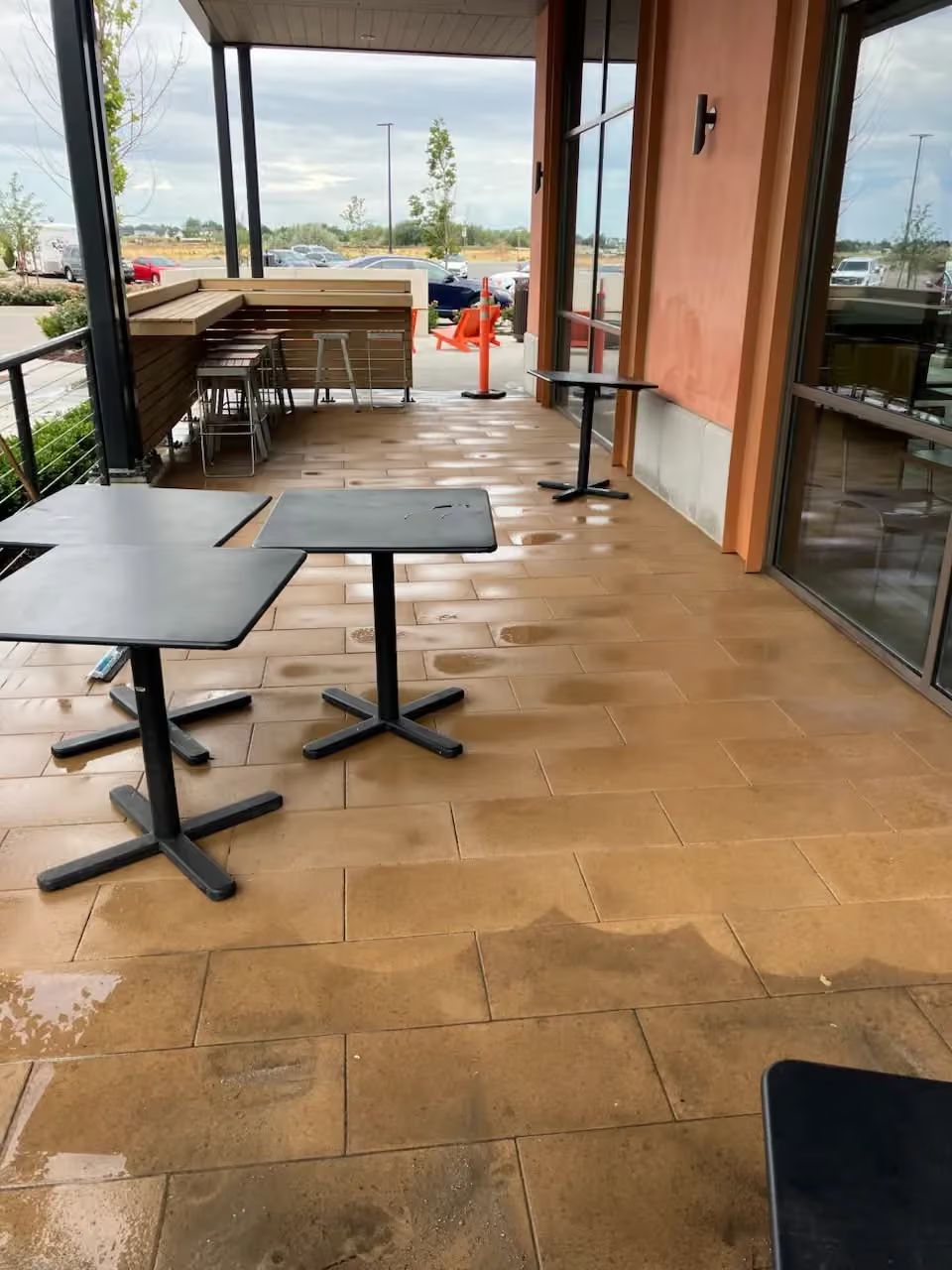 Empty cafe patio with black tables, wooden floor, and a view of the water beyond glass walls