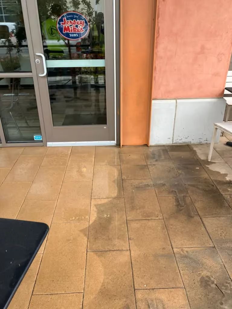 Storefront entrance with glass door, tiled walkway, and orange wall.