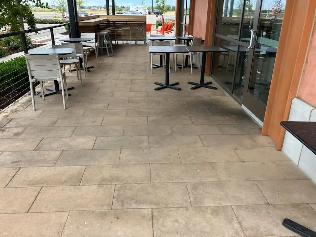 Outdoor café patio with tables, chairs, and glass doors along a tiled walkway.