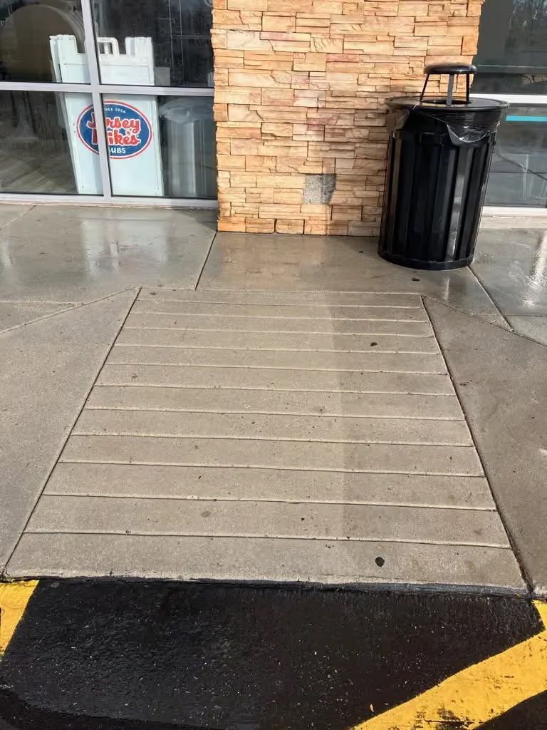 Accessible ramp leading to a store entrance, with yellow curb markings and a black trash can nearby.