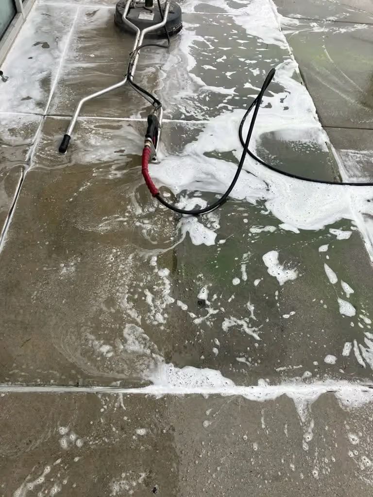 Snow-covered concrete driveway with a black-and-red pressure washer hose and wand on the ground