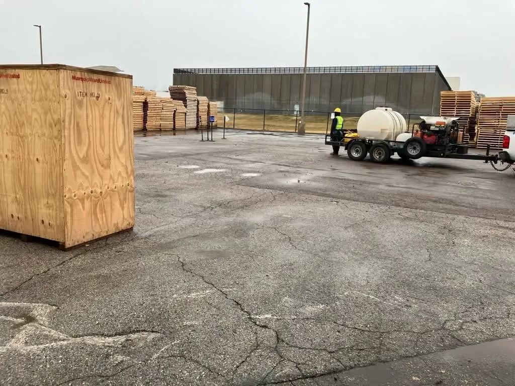 Construction site with large wooden crate, concrete mixer trailer, and workers near a warehouse