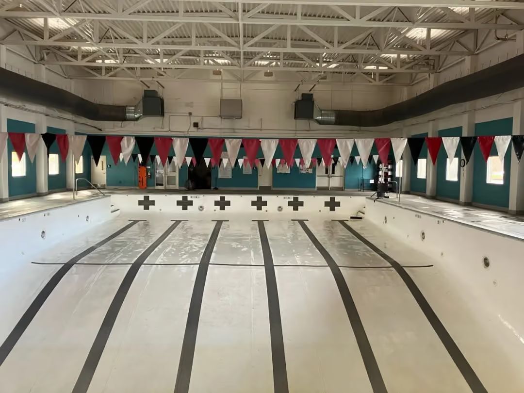 Indoor empty swimming pool with lane markings and red-and-blue pennants overhead