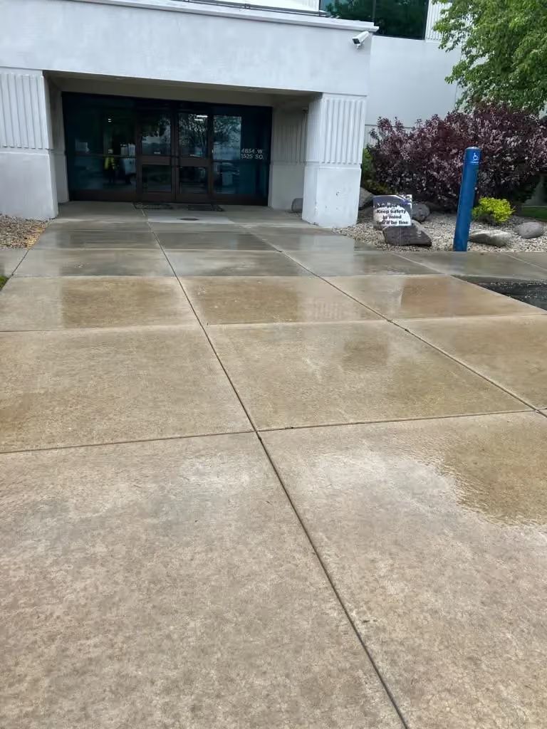 Wet concrete walkway leading to a building entrance with glass doors and white columns