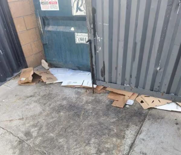 Damaged gate with torn cardboard and debris scattered on a concrete driveway