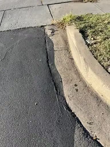 Cracked sidewalk and curb with a patch of asphalt beside a grassy edge
