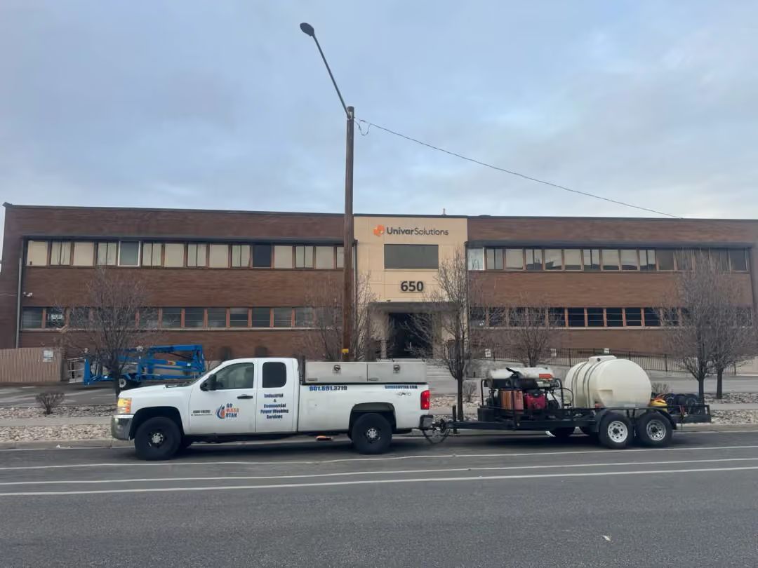 White utility truck towing a tank trailer parked in front of a brick building