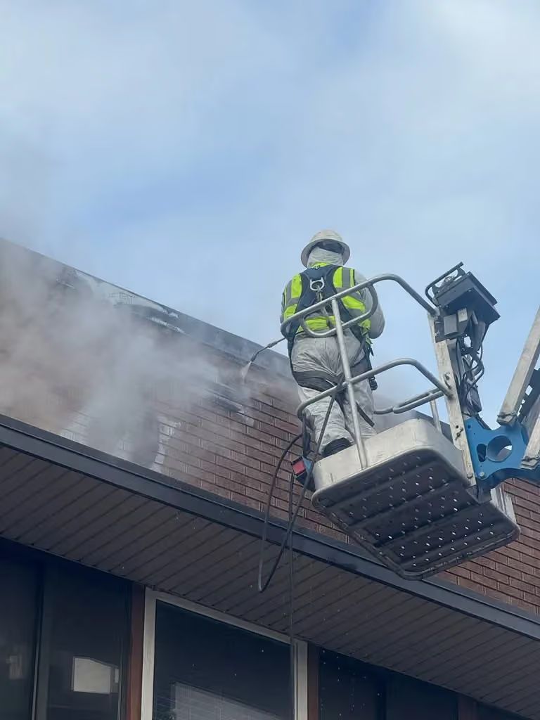 Firefighter on a ladder platform spraying water at smoke rising from a building roof