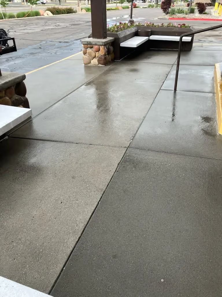 Wet concrete sidewalk with a low ramp and bench by a pillar on a rainy day