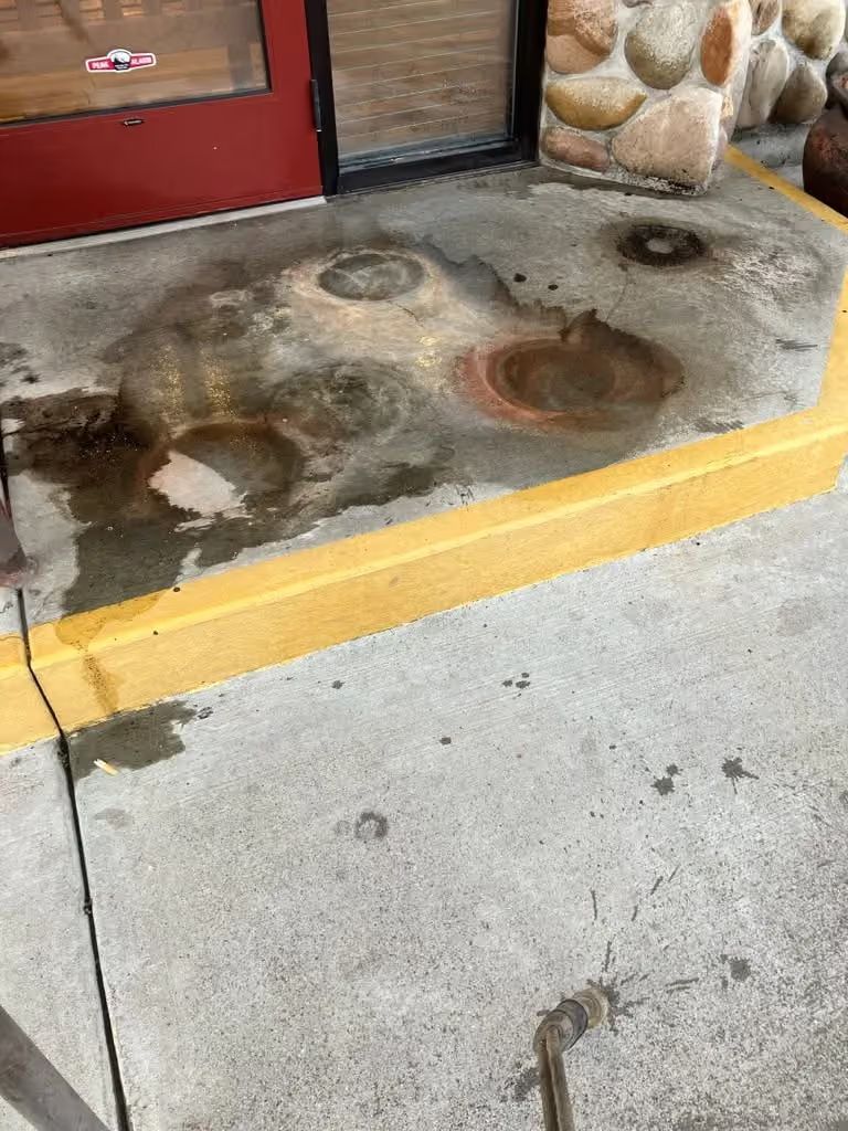 Wet concrete curb with dark stains and puddles beside a red door and stone wall