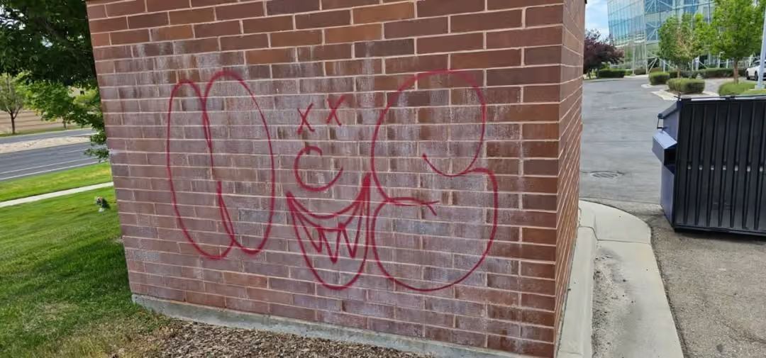 Red graffiti on a brick wall beside a sidewalk and road