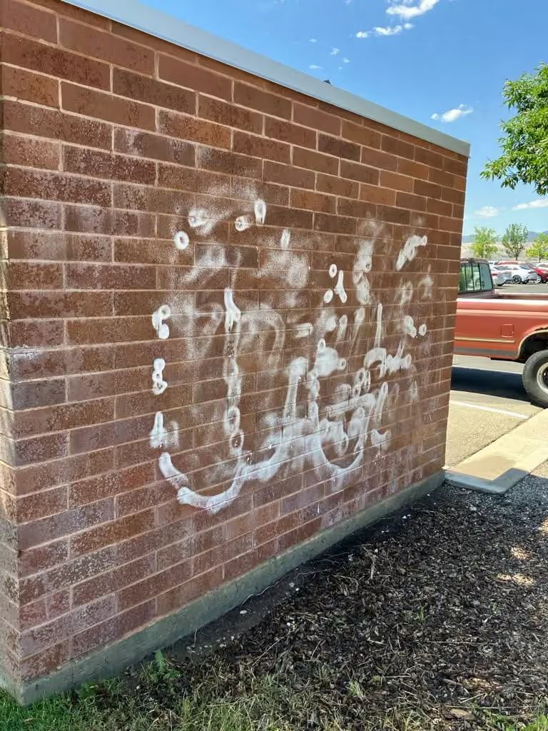 Brick wall with faded white graffiti near a parking lot and a red pickup truck.
