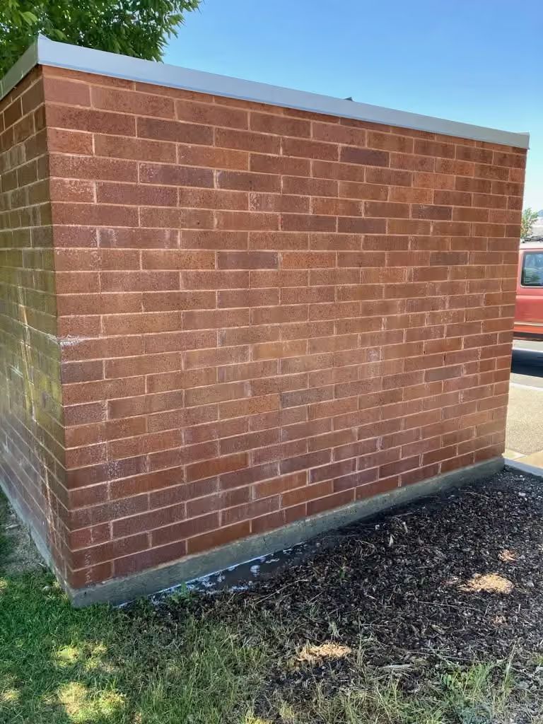 Red brick utility wall beside a grassy area, with a blue trim along the top.