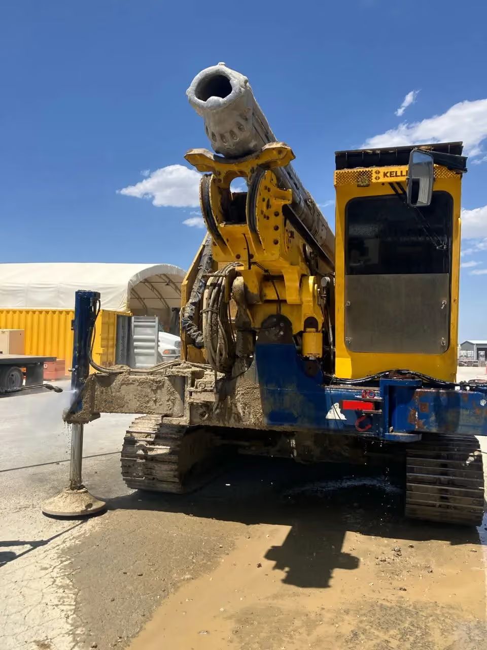 Yellow excavator drilling into pavement at a construction site under a blue sky